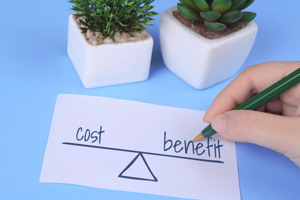 Woman’s,Hand,Holding,Card,With,Words,”cost,Vs.,Benefit”,On